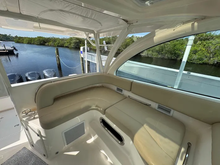  Yacht Photos Pics 2015 Pursuit OS 385 Offshore boat interior with beige seating, docked by a serene waterway.