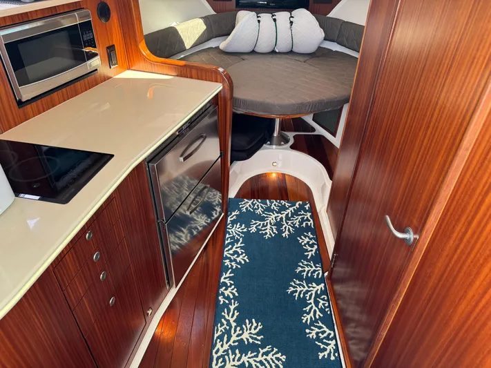  Yacht Photos Pics 2015 Pursuit OS 385 Offshore cabin with kitchenette, bed, and nautical-themed rug.