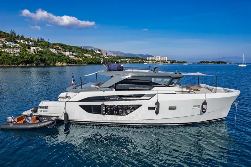 M8-15 Yacht Photos Pics 2023 Bluegame BGX 63 yacht on serene blue waters, coastal backdrop.