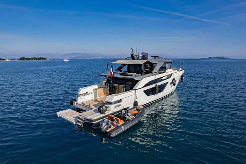 M8-15 Yacht Photos Pics 2023 Bluegame BGX 63 yacht on serene blue waters with a small boat attached.