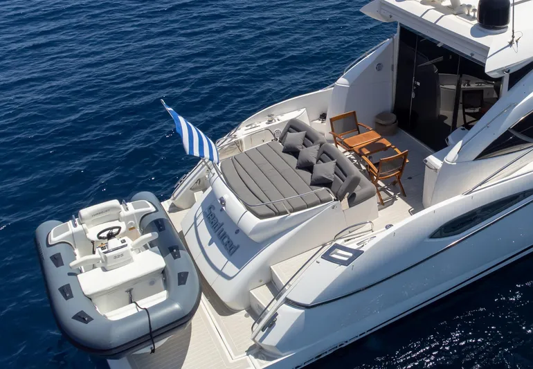 M/y Seaduced Yacht Photos Pics 2009 Sunseeker Predator 52 yacht with inflatable boat, deck chairs, and Greek flag on blue sea.