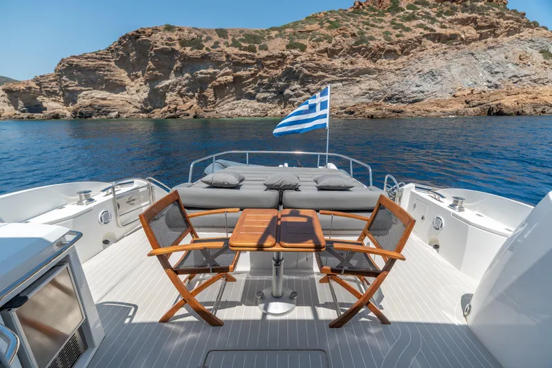 M/y Seaduced Yacht Photos Pics Sunseeker Predator 52 yacht deck with Greek flag, wooden chairs, and scenic rocky coastline.
