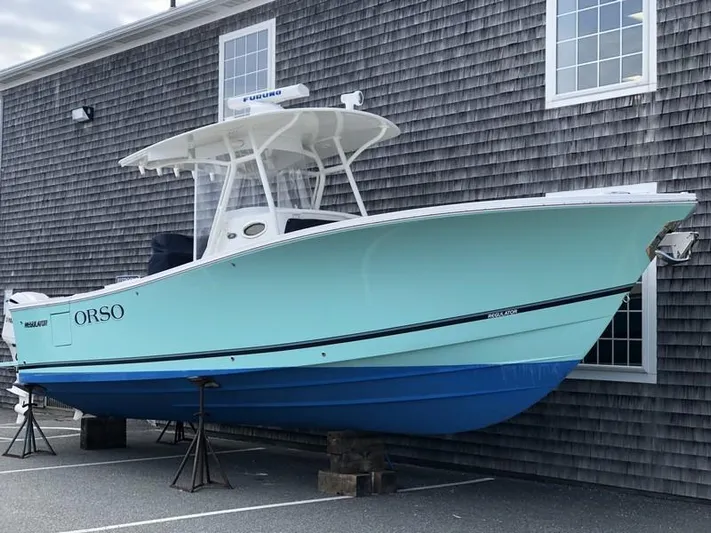 One Knot Yacht Photos Pics 2018 Regulator 31 boat in light blue, docked near a shingled building.