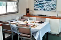 Dining area inside a 2004 Custom Bon Pelley catamaran, featuring a set table and marine artwork.