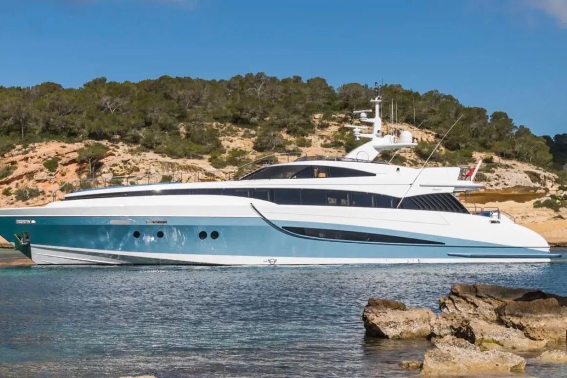 Luxurious 2005 Evolution 110 yacht docked near scenic rocky shoreline.