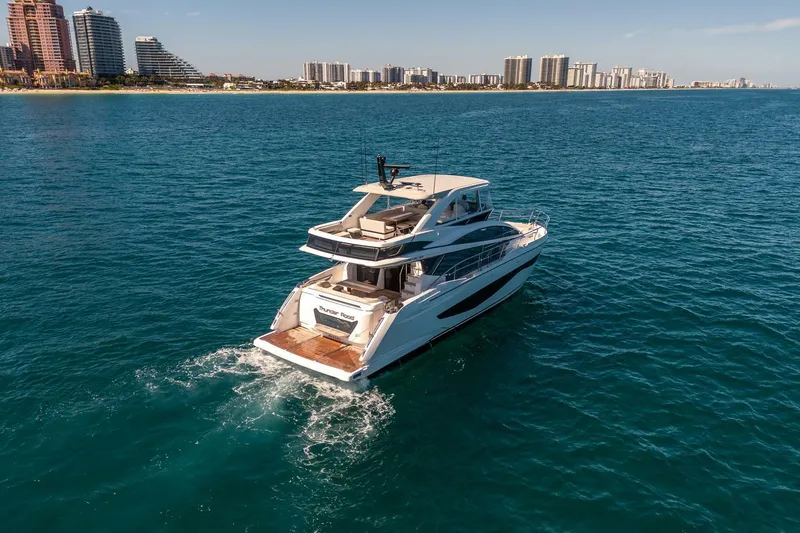 Thunder Road Yacht Photos Pics Luxurious 2023 Pearl 62 yacht cruising on clear blue ocean near city skyline.