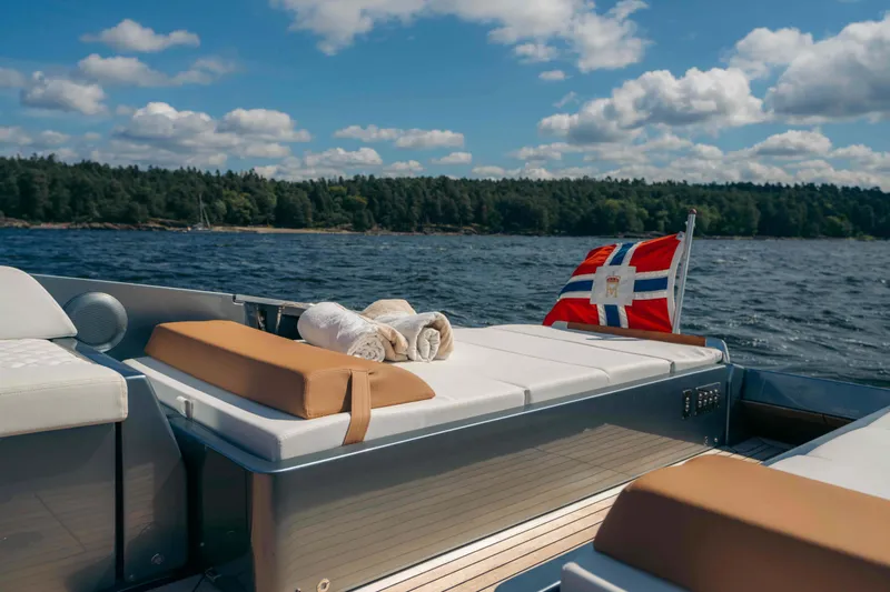  Yacht Photos Pics 2022 Riva Dolceriva yacht with sunbathing deck, towels, and flag on a scenic lake.