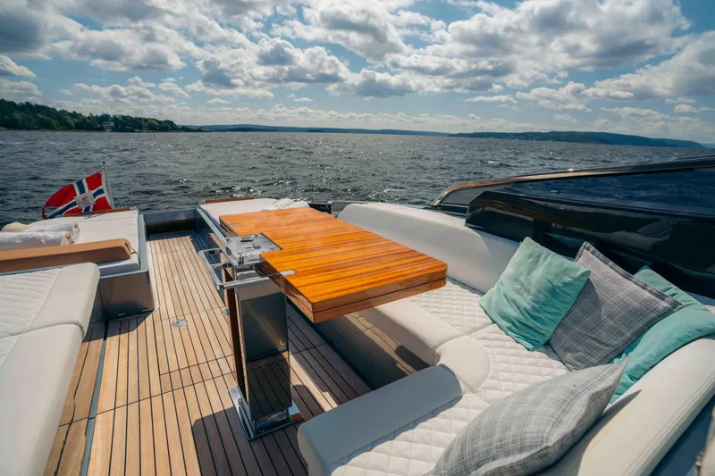  Yacht Photos Pics Luxurious 2022 Riva Dolceriva yacht deck with elegant seating and wooden table, overlooking serene waters.