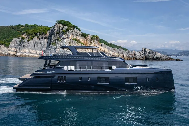 Petite Belle Yacht Photos Pics Luxurious 2025 Sunreef 100 Power yacht cruising near rocky coastline.