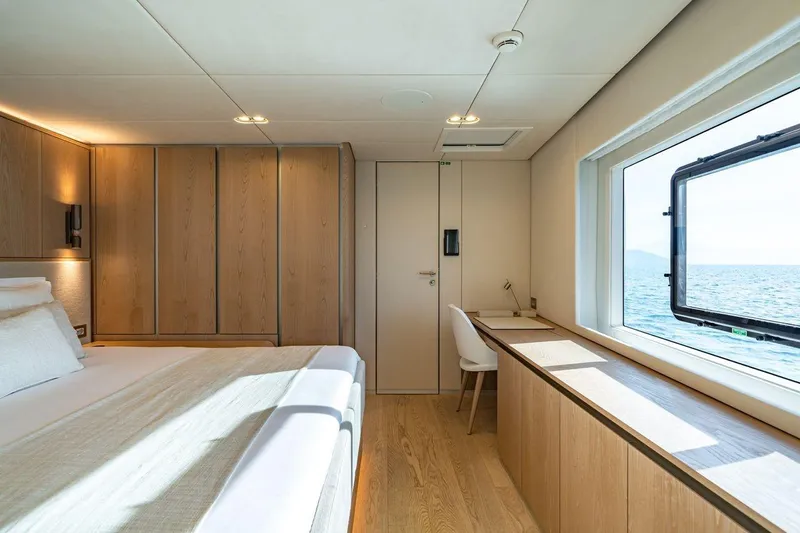 Petite Belle Yacht Photos Pics Luxurious Sunreef 100 Power 2025 yacht bedroom with ocean view, modern wood interior, and desk.