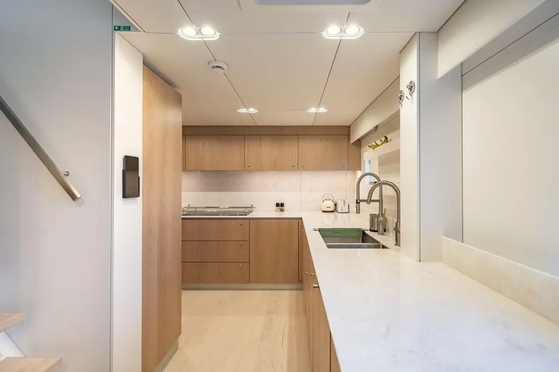 Petite Belle Yacht Photos Pics Modern kitchen interior on 2025 Sunreef 100 Power yacht, featuring sleek wood cabinetry and marble countertops.