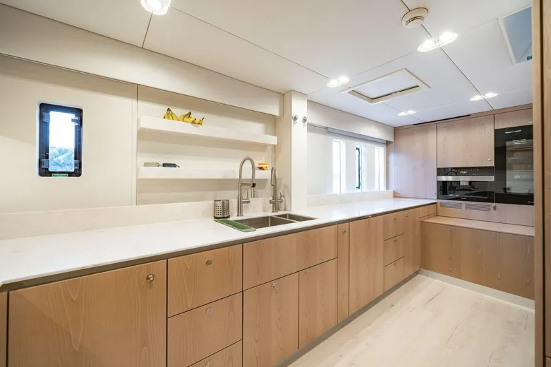 Petite Belle Yacht Photos Pics Modern kitchen interior on 2025 Sunreef 100 Power yacht, featuring sleek wood cabinetry and stainless steel appliances.