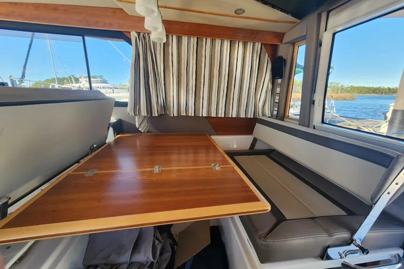  Yacht Photos Pics 2021 Cutwater C-32 CB interior with wooden table, striped curtains, and scenic water view.