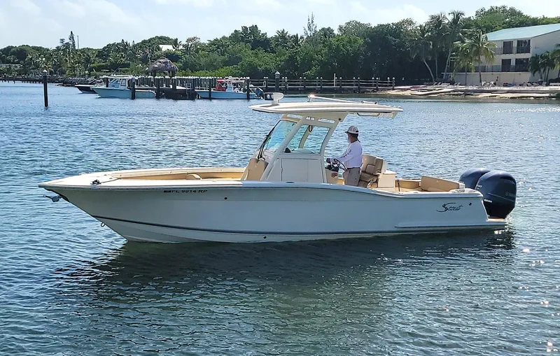  Yacht Photos Pics 2018 Scout 275 LXF boat on water, with a person at the helm, near a shoreline.
