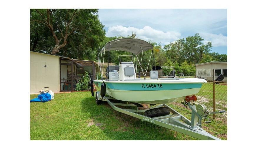 Avid 21 Fusion 2022 boat on trailer in grassy yard with trees and sheds.