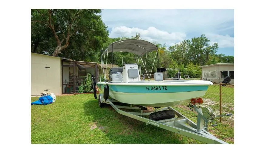Avid 21 Fusion 2022 boat on trailer in grassy yard with trees and sheds.