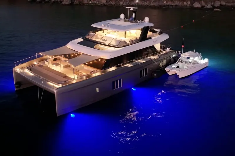 Ellen's Dream Yacht Photos Pics Luxurious 2020 Sunreef 80 Power yacht illuminated at night, docked with a smaller boat.