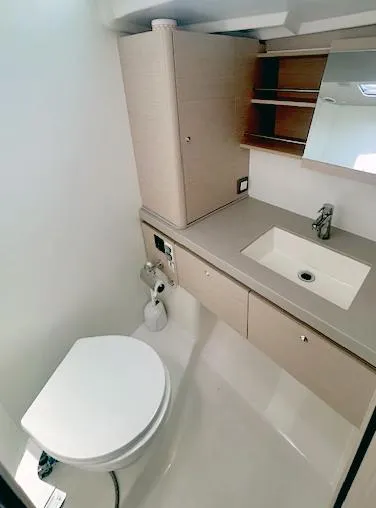 Betwixt Yacht Photos Pics Modern bathroom in 2022 Beneteau Oceanis 51.1 yacht with sink, toilet, and storage.