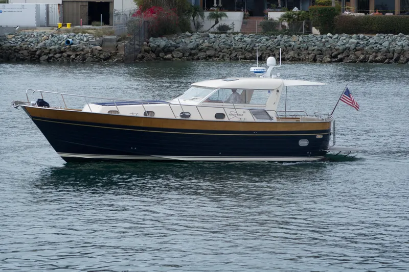 True Grit Yacht Photos Pics 2003 Apreamare 40 yacht cruising near rocky shoreline with American flag.