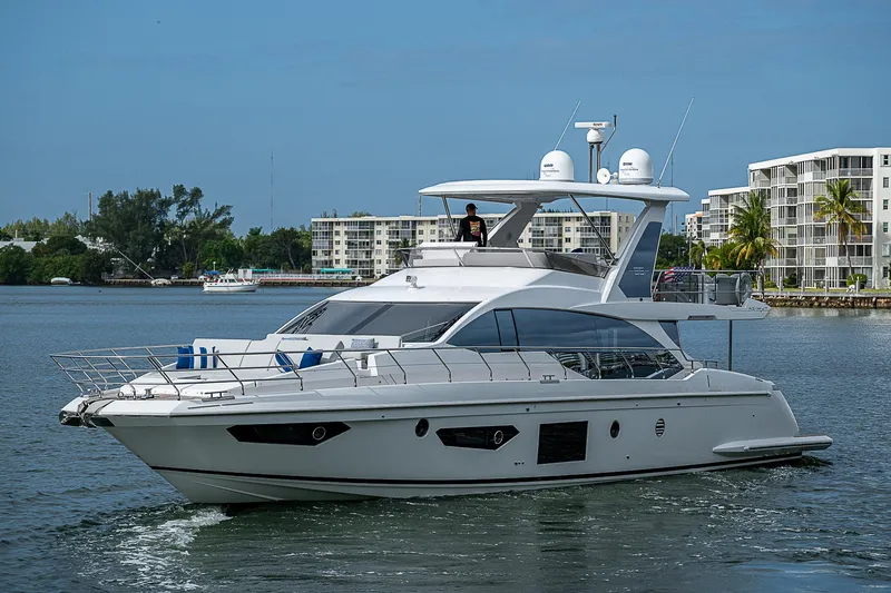 Liquid Asset Yacht Photos Pics 2020 Azimut 66 yacht cruising on a calm waterway near modern buildings.