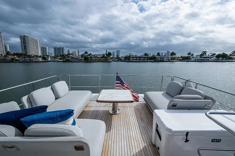 Liquid Asset Yacht Photos Pics Azimut 66 yacht deck with seating, table, and American flag, overlooking waterfront cityscape.