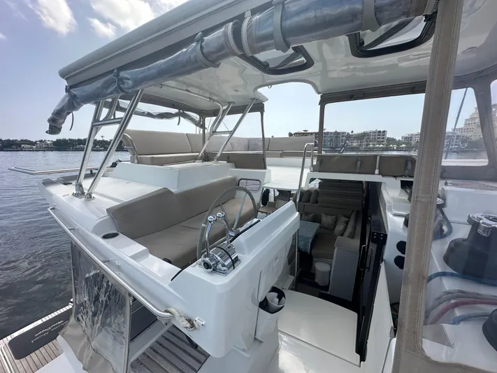 Moon Doggie Yacht Photos Pics 2022 Fountaine Pajot Tanna 47 yacht cockpit with seating and steering wheel, docked by the water.