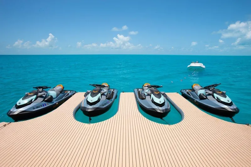 No Bad Ideas Yacht Photos Pics Four jet skis docked on a yacht deck, with a boat in the turquoise sea.