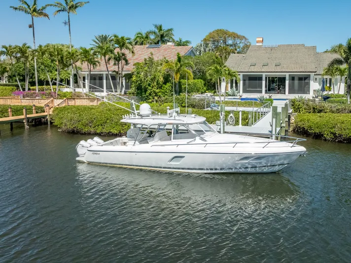  Yacht Photos Pics 2020 Intrepid 407 Cuddy boat docked near waterfront homes, surrounded by lush greenery.