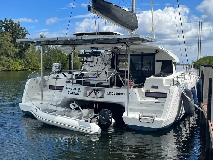 Always Sunday Yacht Photos Pics 2020 Lagoon 42 catamaran docked with dinghy, named "Always Sunday," under a blue sky.