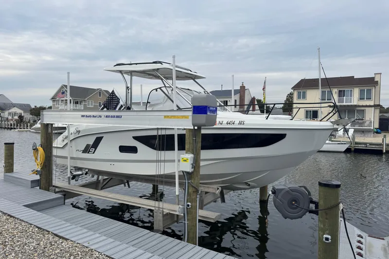  Yacht Photos Pics 2024 Beneteau Flyer 9 SUNdeck on lift at marina, waterfront homes in background.