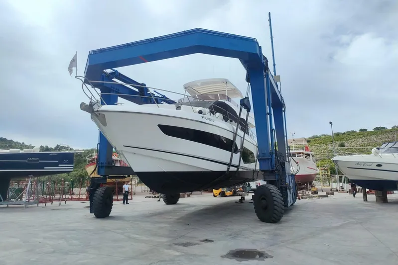 Elixa Yacht Photos Pics 2022 Sunseeker Manhattan 68 yacht lifted by a blue crane in a boatyard.
