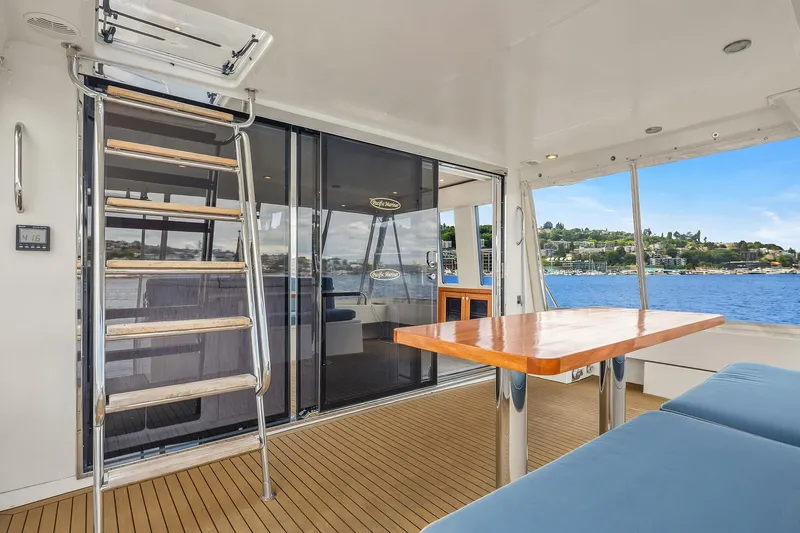 Escencia Yacht Photos Pics 2003 Pacific Mariner Pilothouse yacht interior with wooden table, seating, and ladder, overlooking water.