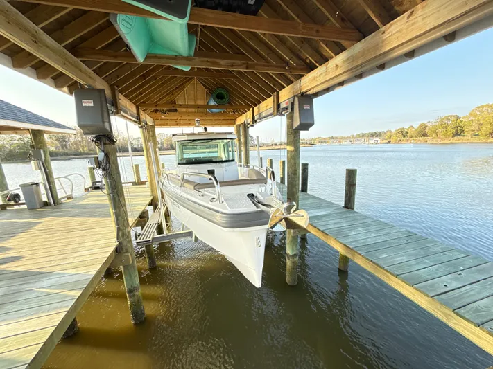 Yacht Photos Pics 2019 Axopar 28 CABIN boat docked under wooden shelter on a serene lake.