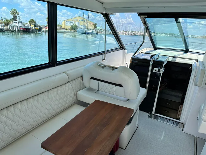  Yacht Photos Pics 2023 Regal Grande Coupe interior with white seating and wooden table, overlooking marina.