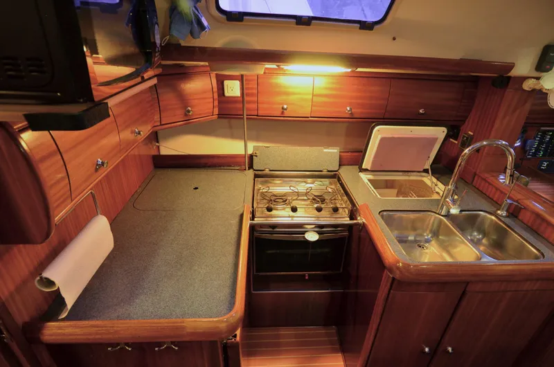 Footloose Yacht Photos Pics Interior of a 2003 Bavaria 49 yacht kitchen with wooden cabinetry and modern appliances.