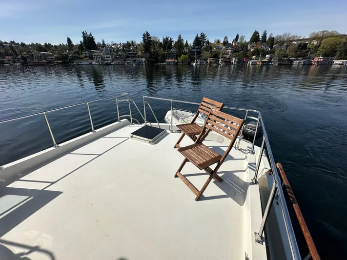  Yacht Photos Pics 1982 Tollycraft Tri Cabin boat deck with wooden chairs, overlooking calm water and shoreline.