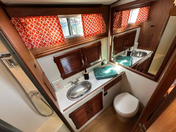  Yacht Photos Pics 1982 Tollycraft Tri Cabin bathroom with sink, toilet, mirror, and red-patterned curtains.