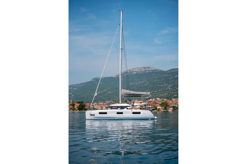 Yacht Photos Pics 2024 Lagoon 450 F catamaran sailing on calm waters with scenic mountain backdrop.