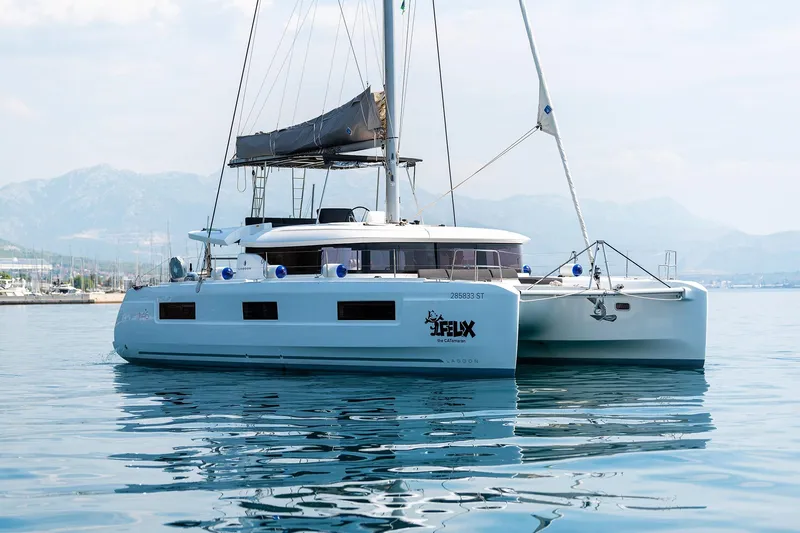  Yacht Photos Pics 2024 Lagoon 450 F catamaran sailing on calm waters with mountainous backdrop.