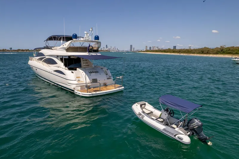 Shhmic Yacht Photos Pics 2001 Sunseeker Manhattan 74 yacht anchored with a small boat in clear blue water.
