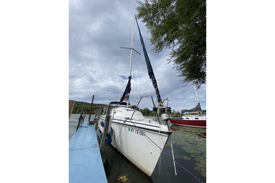 1990 Hunter 27 sailboat docked on a cloudy day, surrounded by water and greenery.