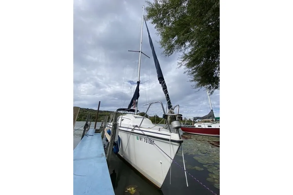 1990 Hunter 27 sailboat docked on a cloudy day, surrounded by water and greenery.