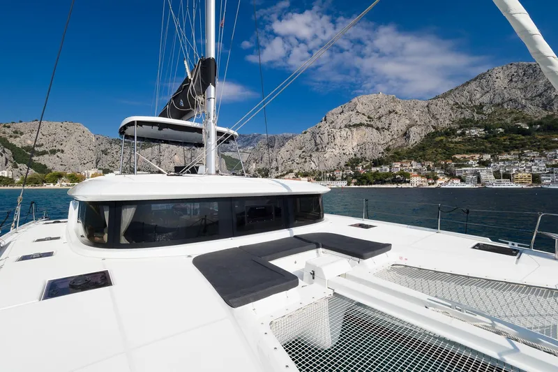 Almissa Yacht Photos Pics 2023 Lagoon 46 catamaran with scenic coastal mountain backdrop under clear blue sky.