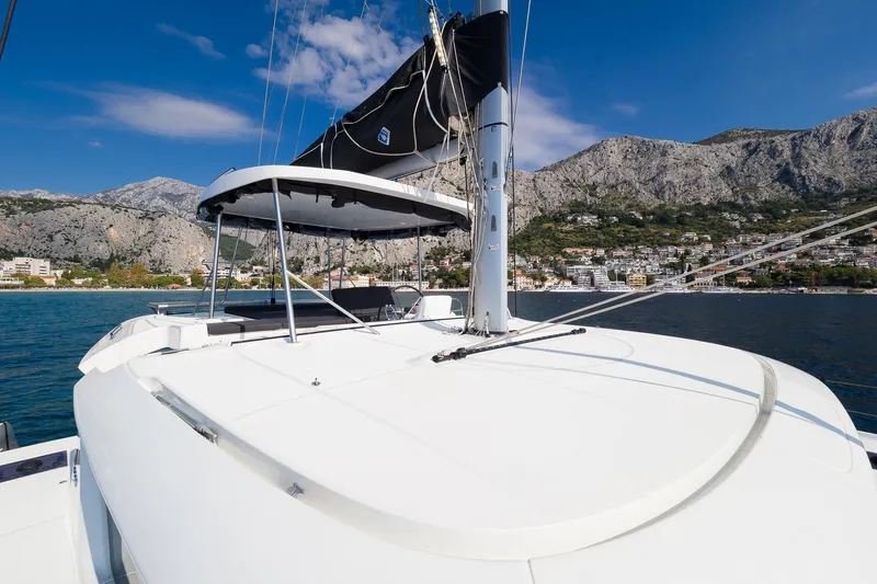 Almissa Yacht Photos Pics 2023 Lagoon 46 catamaran sailing near coastal mountains under clear blue sky.