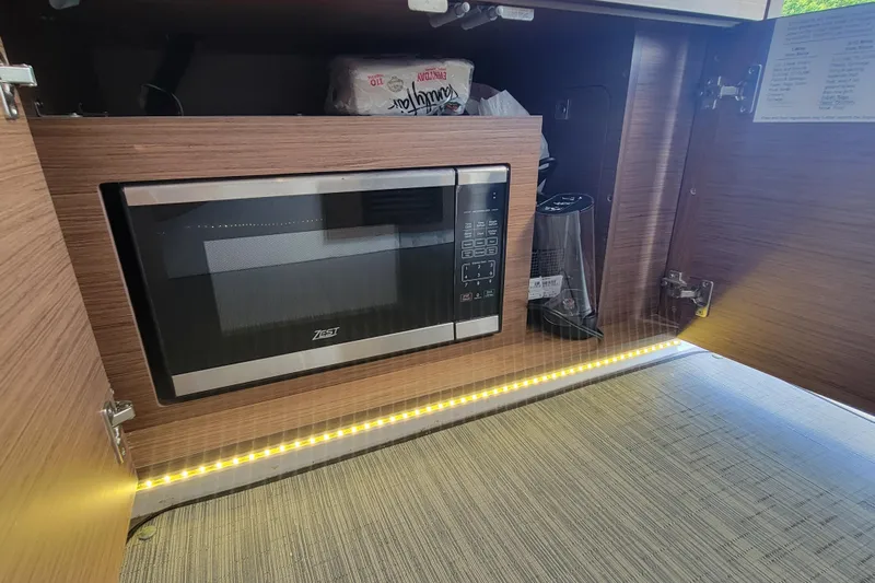 Tagwood Bbq Yacht Photos Pics Microwave in Jeanneau NC 895 boat kitchen, 2023 model, with wooden cabinetry and LED lighting.