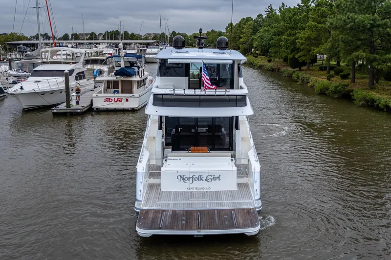 Norfolk Girl Yacht Photos Pics 2023 Maritimo M55 yacht cruising in a marina, surrounded by other boats and lush greenery.
