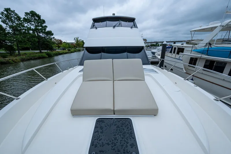 Norfolk Girl Yacht Photos Pics 2023 Maritimo M55 yacht with cushioned deck seating, docked by a scenic waterway.