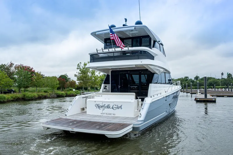 Norfolk Girl Yacht Photos Pics 2023 Maritimo M55 yacht docked, rear view with American flag, lush greenery in background.