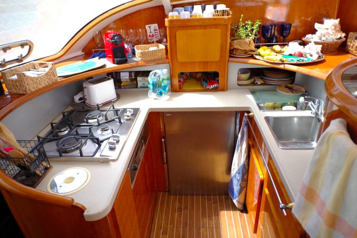 Compact kitchen in a 2004 Privilege 49 yacht, featuring stove, sink, and wooden cabinetry.