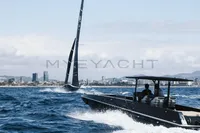 Speedboat cruising near a sailboat on open water, cityscape in the background.